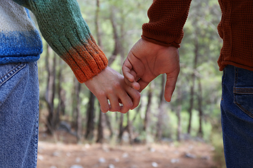 Cropped shot of young couple holding hands on the hike in the woods. Close up, copy space, forest landscape background.