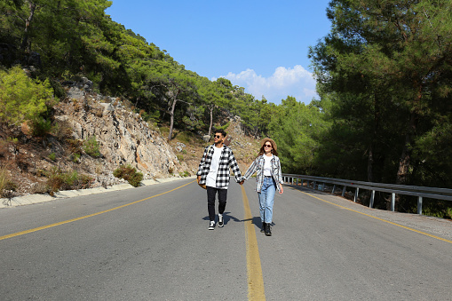 Romantic scene with happy hipster couple in checked flannel shirts walking down the empty switchback road. Young people holding hands. Close up, copy space, background.