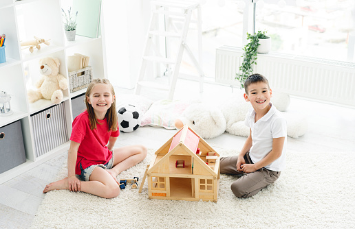 Happy kids having fun with wooden dollhouse in play room, top view