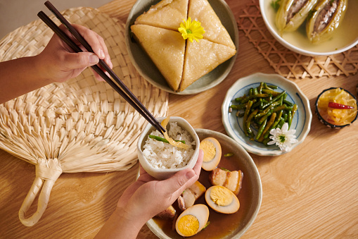 Hands of person having white rice with green beans, braised pork and square cake for holiday dinner