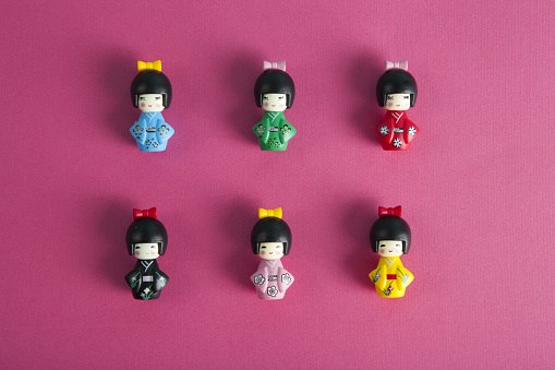 a collection of 6 wooden kokeshi dolls aligned in rows and columns on a fushia background. Minimalist, trendy still life photography.