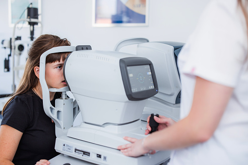 Teenage girl sitting on an eye pressure gauge at doctor's office