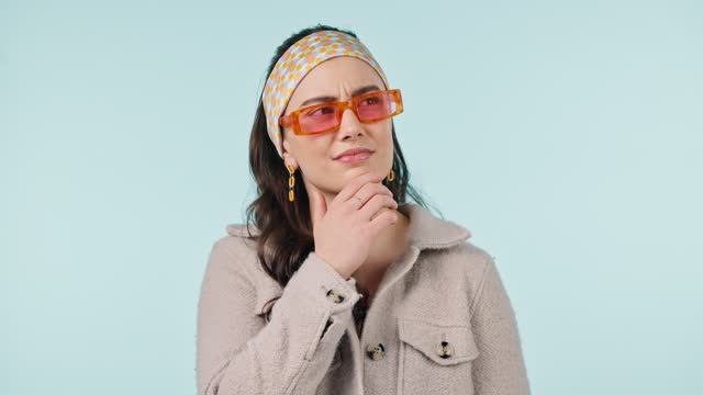 Studio, fashion sunglasses and face of woman thinking about clothes decision, trendy apparel or outfit choice. Problem solving style ideas, apparel plan and person with glasses on blue background