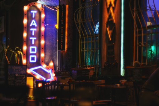 Izmir, Turkey - September 1, 2023: Nestled in the narrow streets of Alsancak, a tattoo shop stands out with its neon lights spelling \