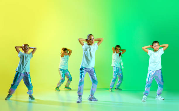 istock Cute talented children dressed in style clothes with bright glittered makeup performing new dance tricks synchronous movements over gradient background. 1740921698