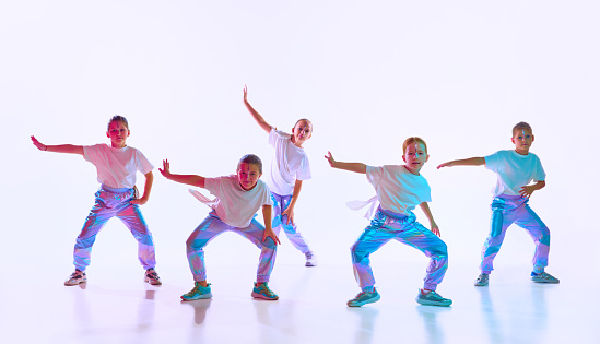 Team of girls wearing style clothes with trendy, creative hairstyle dancing synchronous in choreography class over gradient background in neon light. Concept of hobby, music, motion, childhood.