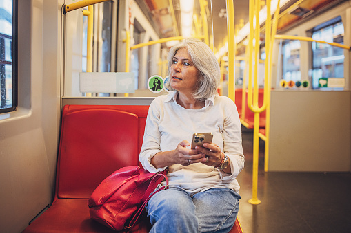 Mature woman using smart phone while riding on a subway train in Vienna.
