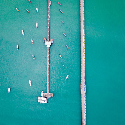Aerial drone view of 2 bridges with tour boats anchored around at Ao Chalong Bay. One is a local pier with a dolphin floor pattern and another one is a vehicle way to Chalong Pier in Phuket, Thailand.