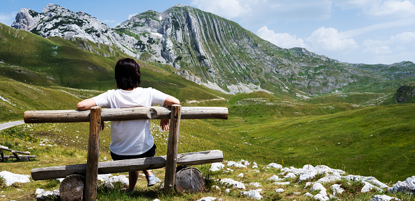 Girl sitting on wooden bench in mountains of Montenegro. Young girl resting in National park Durmitor with scenic nature view