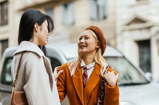 Young stylish women talking while meeting outdoors on the street.