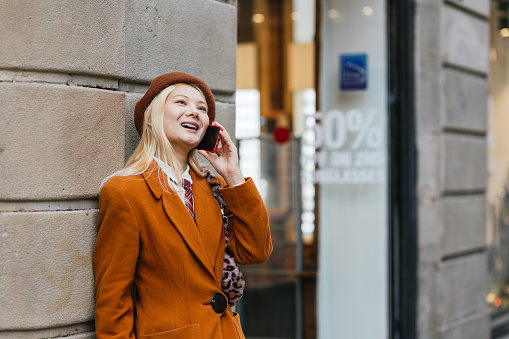 Young Asian woman smiling while talking on the phone standing outdoors on the street. Technology concept.