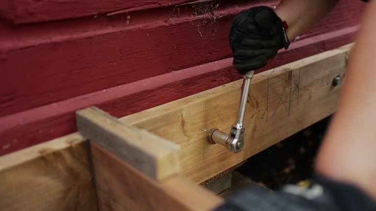 Woman attaching a wooden deck frame to a house using a wrench