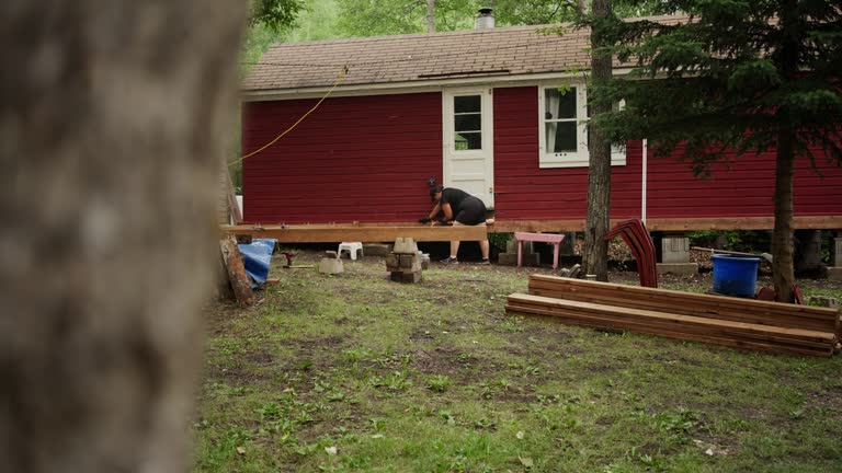 Woman using a wrench to attach a deck frame to a wooden house