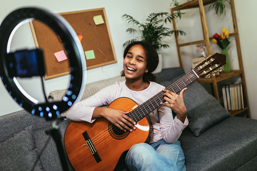 African American woman playing a guitar with the help of online tutorials.