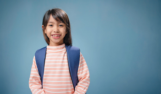 A little girl is carrying a school bag and smiling.