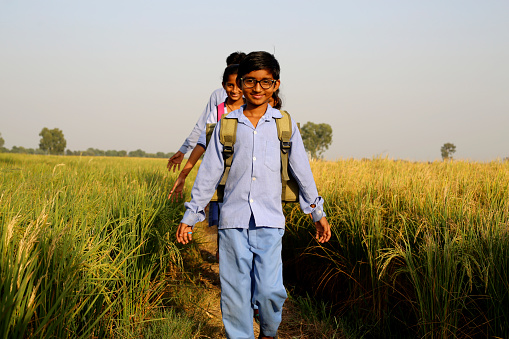 Elementary age school students walking in a row on country road after school vacation portrait together outdoor in nature wearing school uniform.