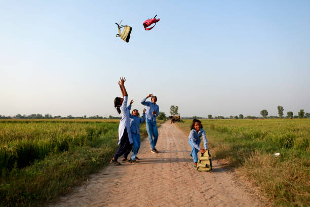 School students wearing school uniform throwing school bag in mid-air after vacation playful portrait outdoor in nature near green field during springtime.