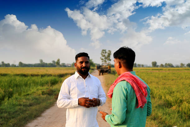 Two farmer of Indian ethnicity discussing something near green field during springtime under the beautiful cloudscape outdoor portrait close up.