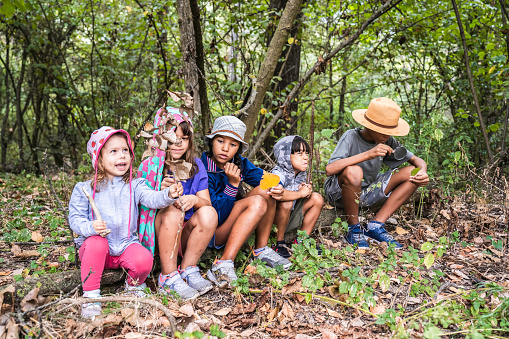 Group of curious happy school kids in casual clothes exploring nature and forest together - The children holding the finds found in the woods in their hands - Nature and wildlife concept with children