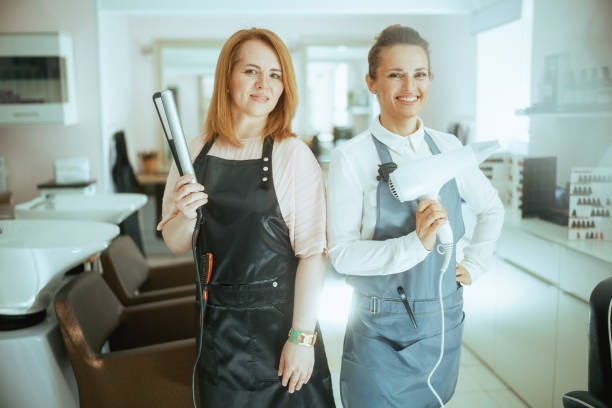 ヘアスタジオのエプロンを着た幸せな2人のヘアサロン従業員 - frizzy human hair hairdresser hair dryer ストックフォトと画像