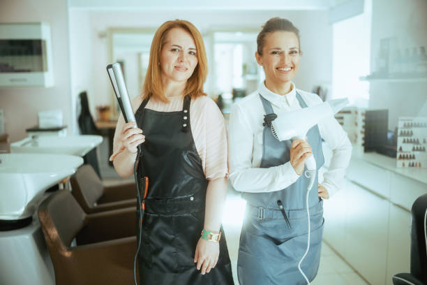 happy two hair salon employees in aprons in hair studio - frizzy human hair hairdresser hair dryer imagens e fotografias de stock