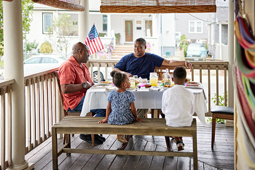 Full length view of family members relaxing and talking at dining table on veranda as they celebrate summertime holiday in Rockaway Beach, Queens.