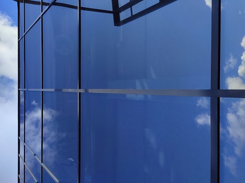 Windows of a modern glass building. Looking up at the commercial buildings in downtown. Modern office building against blue sky. Reflection of sky and clouds in the glass facade of a building