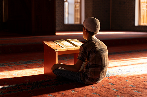 A boy reading the Qur'an in a mosque. A boy praying in a mosque. Sacred places for Muslims.