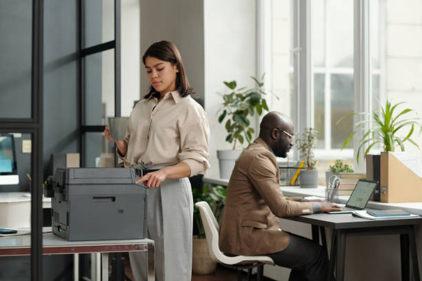 istock Young businesswoman with cup of coffee pressing button on copier panel 1741050687