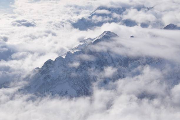 istock Dreamy aerial view of snowcapped alpine mountain range peaking through heavy clouds 1741051314