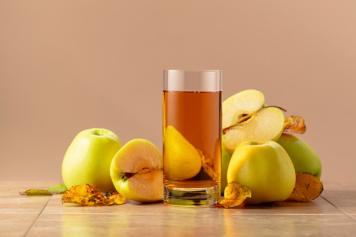 Apple juice and ripe apples with dried-up leaves. Beige background with copy space.
