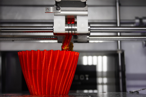 Close-up on a 3D printer, creating a three dimensional object, a red cup