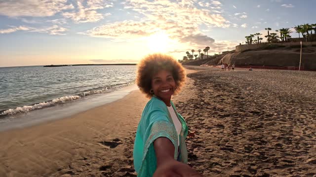 One afro multiracial young beautiful woman holding and looking at the camera taking a selfie at the beach enjoying summer time outdoor on holiday.