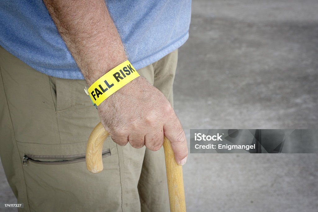 Fall Risk Bracelet And Wooden Cane Fall risk bracelet around an elderly man's wrist while walking with a wooden cane Falling Stock Photo