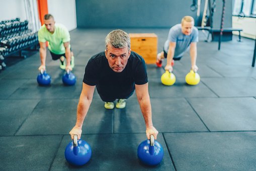 Group of sportspeople in gym exercising push-ups with kettlebell