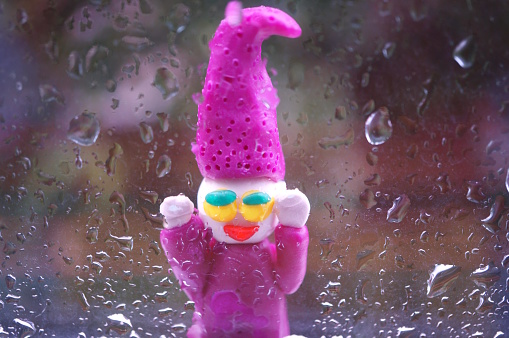 A toy gnome made of plasticine on the background of a wet window.