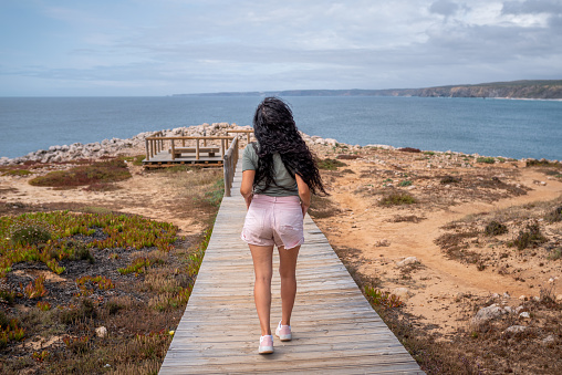Rear view of a Young woman walking along a wooden footbridge in Pontal da Carrapateira, Algarve. Portugal