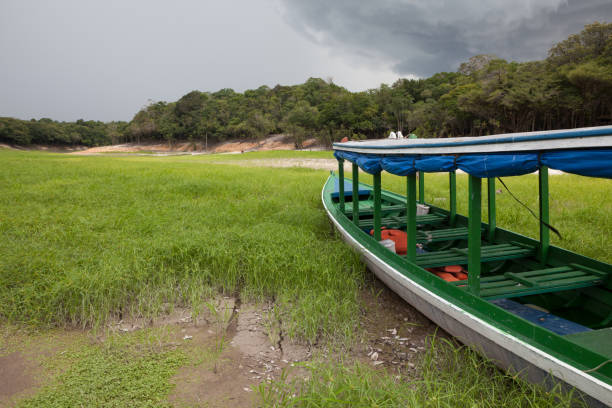 Boat stranded on dry river in extreme drought in the Amazon Rainforest, the largest tropical forest in the world. Concept of climate change, global warming, environment, ecology, disaster, weather.