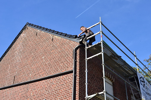 Leuven, Flemish-Brabant, Belgium - October 17, 2023: complete new roof tiles on roof. Slovak roofer lays last roof tiles on a 100 years old detached house on a sunny Autumn week day