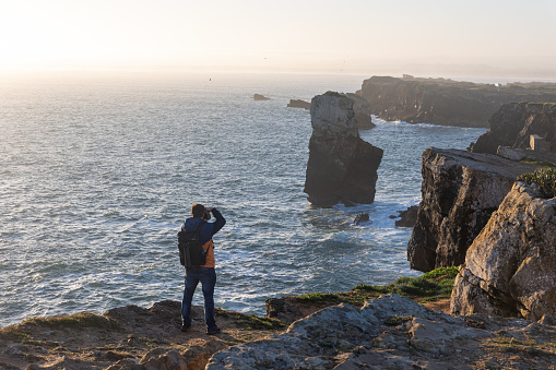 Peniche, Portugal, 15 March 2023 - A man photographer takes photos of the sea and rocks standing on top of a cliff. Mid shot