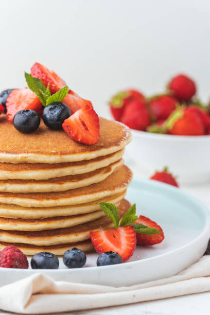 istock Stack of fresh pancakes with strawberries and blueberries drizzled with maple syrup and honey. Healthy traditional American breakfast on the white background 1741246597