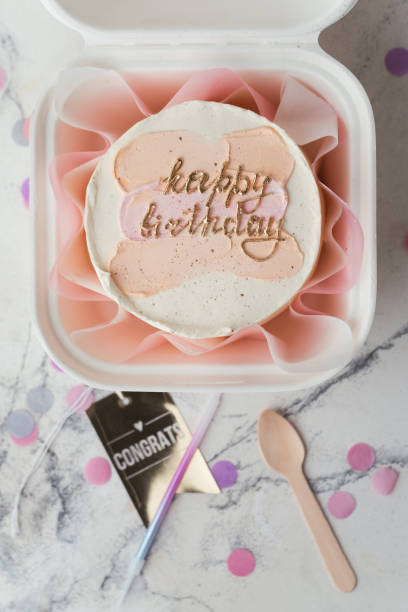 piccola torta di compleanno in una confezione regalo bianca con cucchiaio e candelina. torta bento alla moda in stile coreano con scritta buon compleanno e macchie di crema pastello rosa in cima. posa piatta - box cake food lunch foto e immagini stock