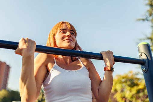 Woman is doing top position chin ups on straight bar