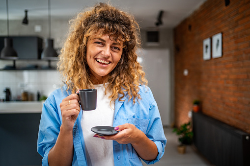 A young woman dressed in pajamas is enjoying her morning coffee in her apartment