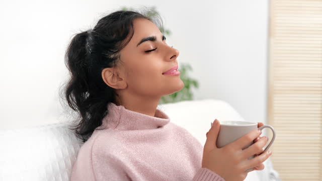 Relaxed young Muslim beautiful woman enjoy morning coffee tea resting at white room day light home