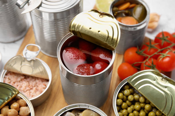 istock Open tin cans with different preserved products on wooden board, closeup 1741325260