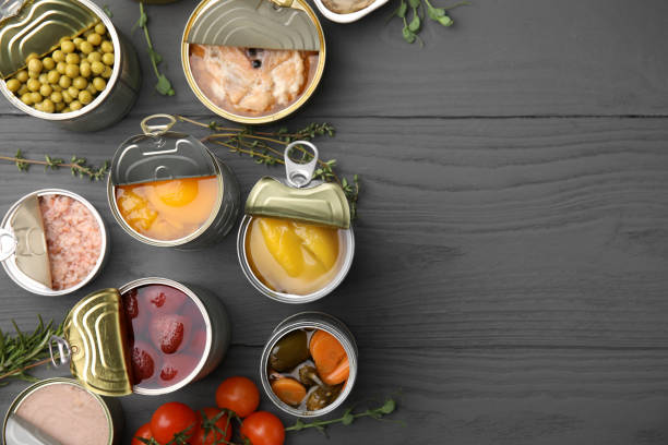 istock Open tin cans with different products on gray wooden table, flat lay. Space for text 1741327608