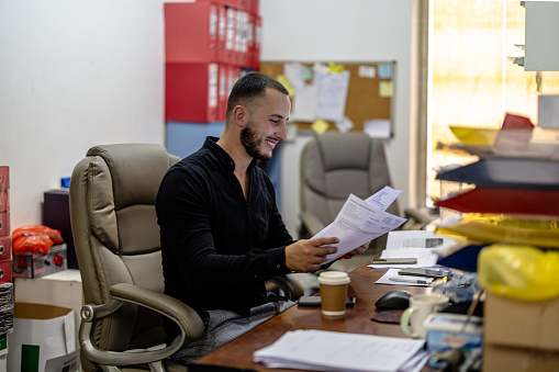 In the professional workspace, a dedicated young businessman exemplifies efficiency and competence as he meticulously attends to the finalization and organization of paperwork