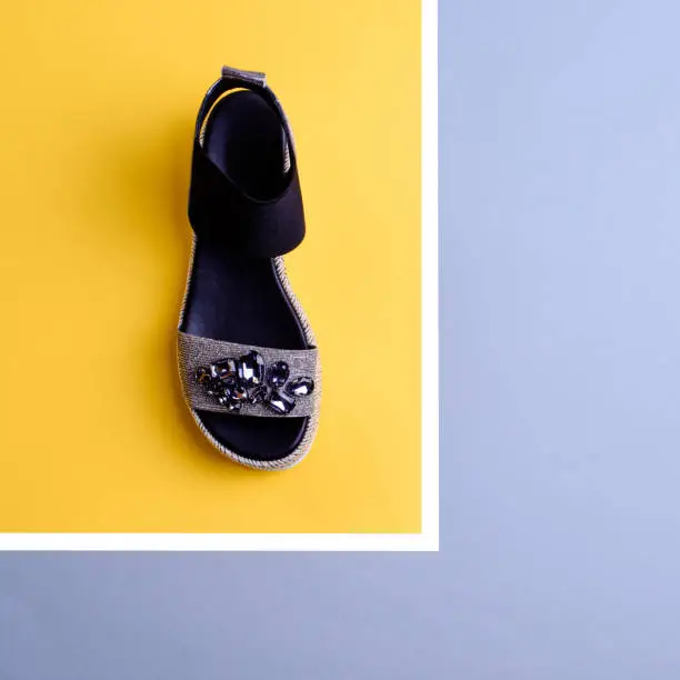 Stylish black-silver sandal decorated with a scattering of rhinestones on yellow and grey background. Fashion blog. Discount, season sales. Footwear retail, orthopedics ,e-commerce outlet store