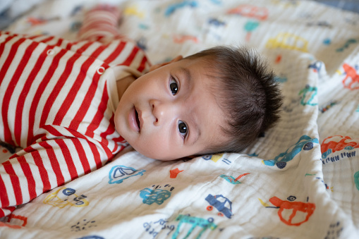 Portrait of beautiful multiracial five month old baby boy in red and white striped crawlers on bed at home